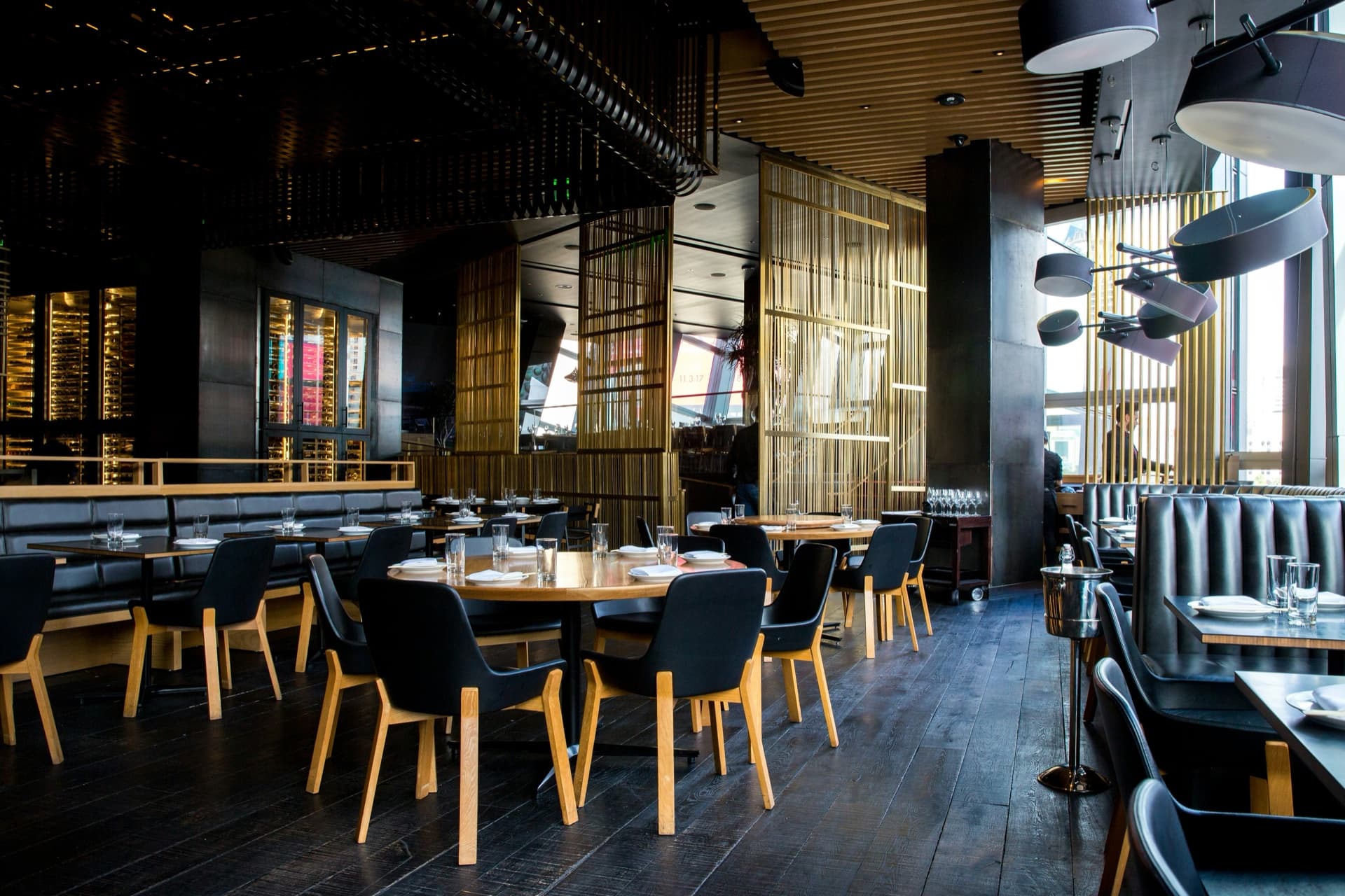 Nowoczesne wnętrze restauracji z ciemnymi skórzanymi fotelami, drewnianymi stołami i złotymi przegrodami